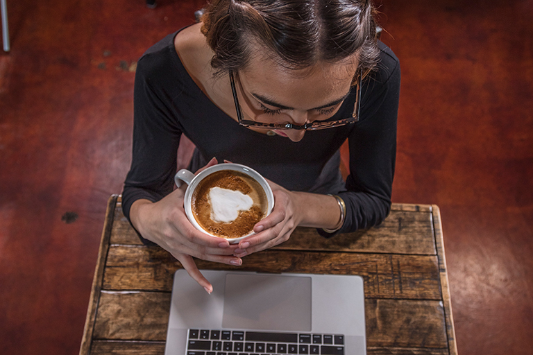 woman with a fancy espresso looking at her laptop