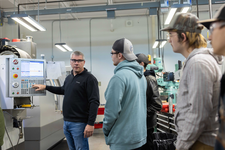 instructor teaching some students about a machine in the robotics lab