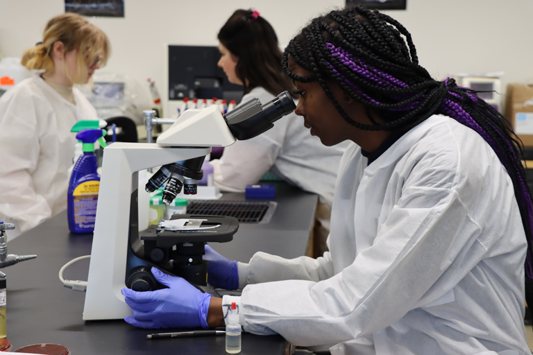 student in a lab looking through a microscope