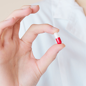 Close up of hand holding red and white pill.