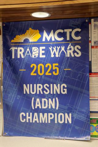 the Trade Wars 2025 Nursing (ADN) Champion banner hanging from the ceiling