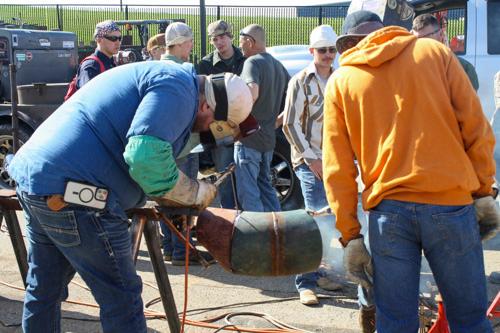 two students working on a pipe outside while others watch