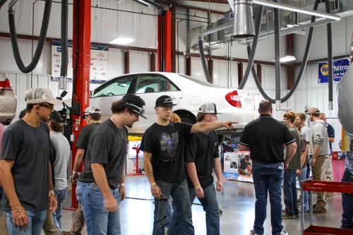 group of students standing around a garage at MCTC with a white car in the air