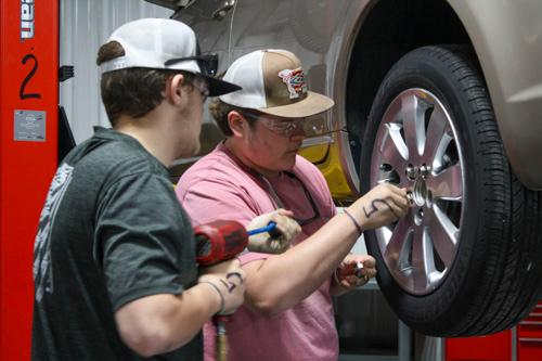 two students working on the wheel of a car