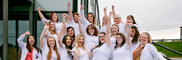 Group of nursing students dressed in white lab coats jumping and raising their hands happily after finishing their program.