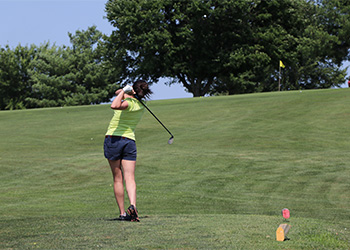 Female golfer in neon green shirt swinging a golf club.