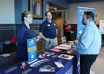 Allied health program instructors speaking with a student at the nursing table at the College to Career Showcase.