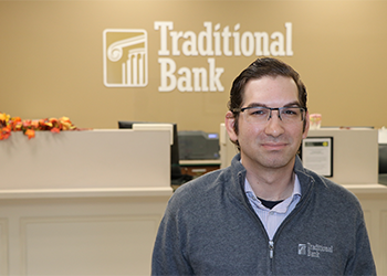Roca standing in front of the Traditional Bank logo at his workplace.