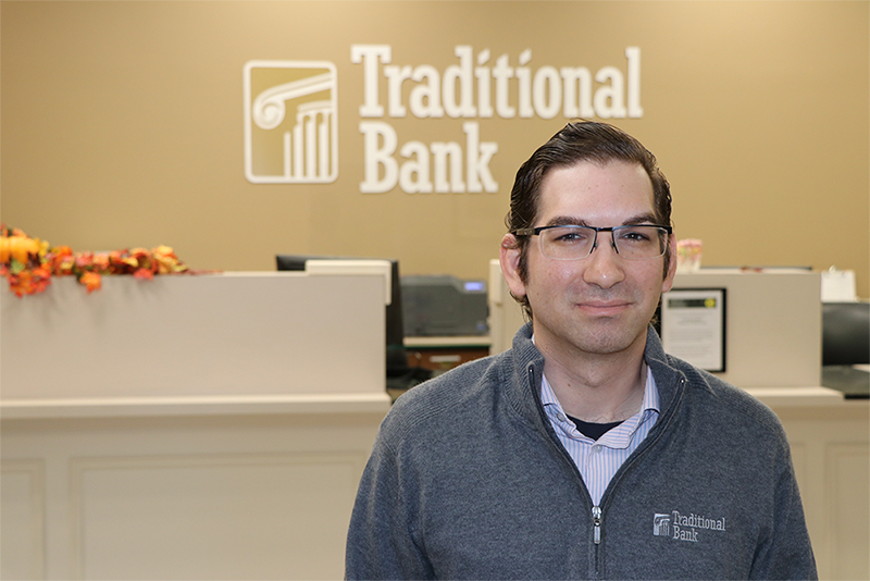 Roca standing in front of Traditional Bank logo at his workplace.