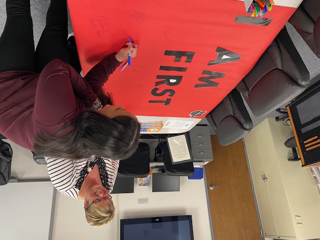 staff signing the "I am first" banner