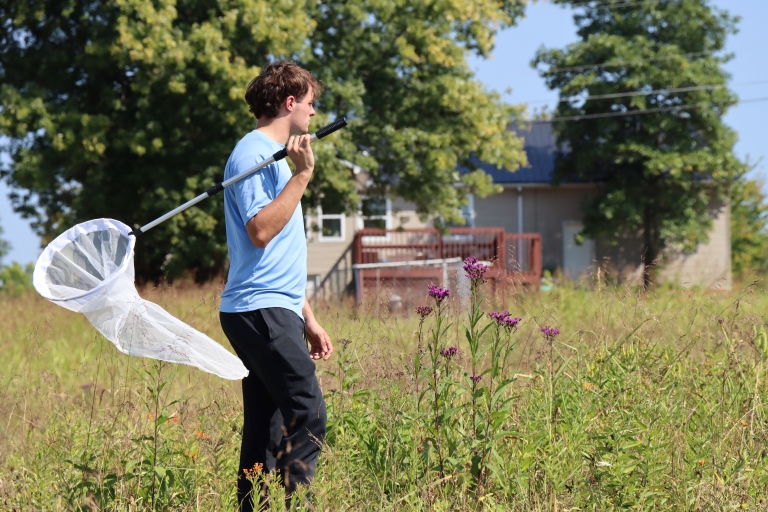 student in a field of flowers with a net