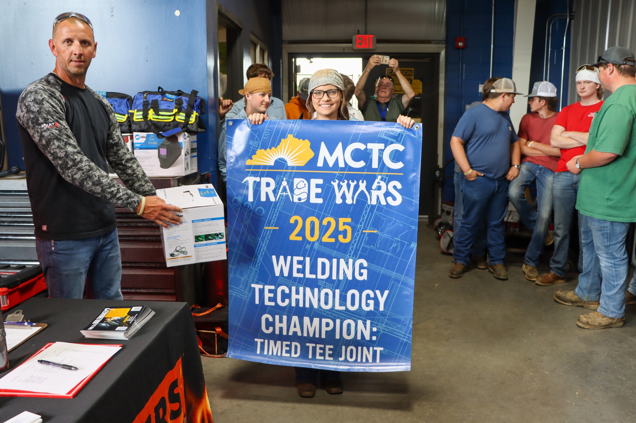female students holding a banner showing that she is the MCTC Trade Wars 2025 Welding Technology Champion for Timed Tee Joint