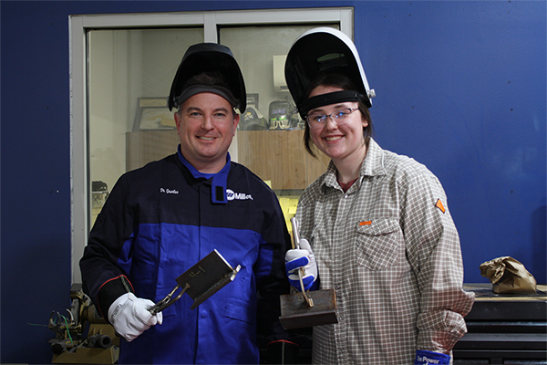 MCTC Welding student Morgan Wells posing for a photo with KCTCS president Dr. Ryan Quarles; both wearing open welding helmets and welding jackets.