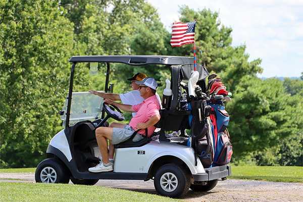 Two men on golf cart with a small United States flag on the top.