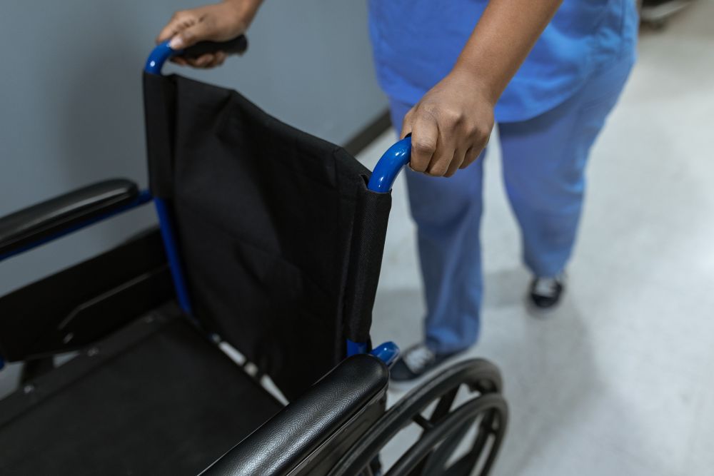 Hands pushing an empty wheelchair.