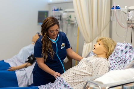 MCTC nursing student using a stethoscope on a mannequin in the nursing lab